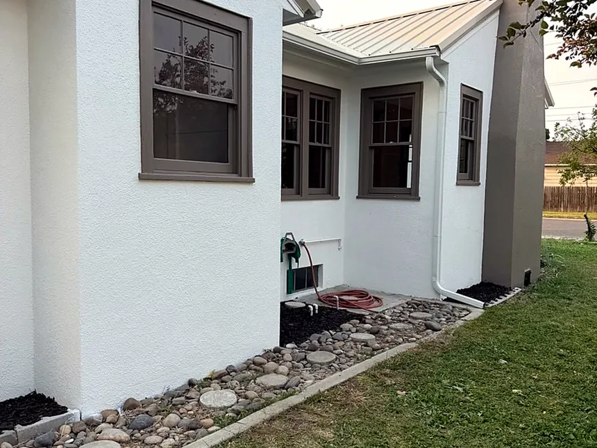 Finished exterior side of a stucco home with new windows, drainage rock and landscaping