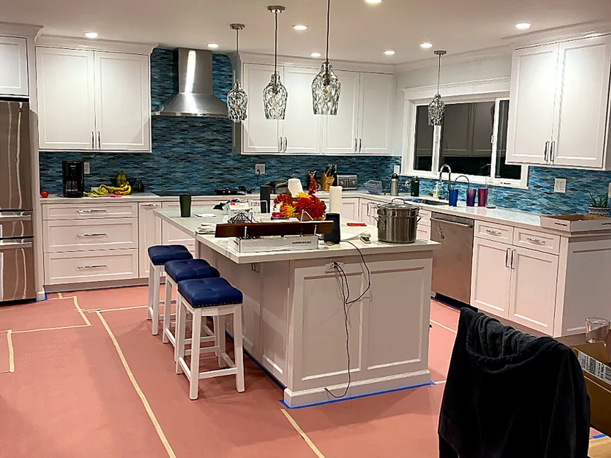 Wide view of a completed kitchen island with seating, pendant lights and a glass tile backsplash
